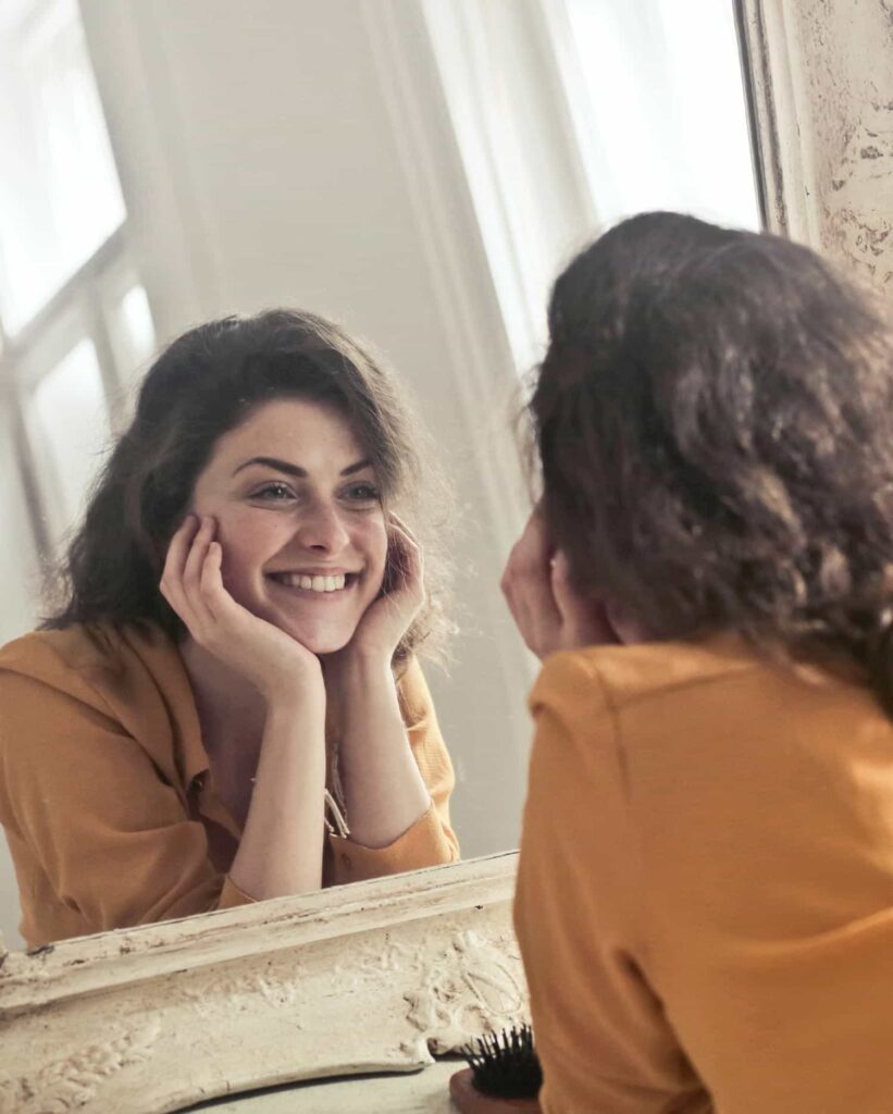Eine junge Frau liegt vor einem Spiegel und lächelt ihr Spiegelbild an