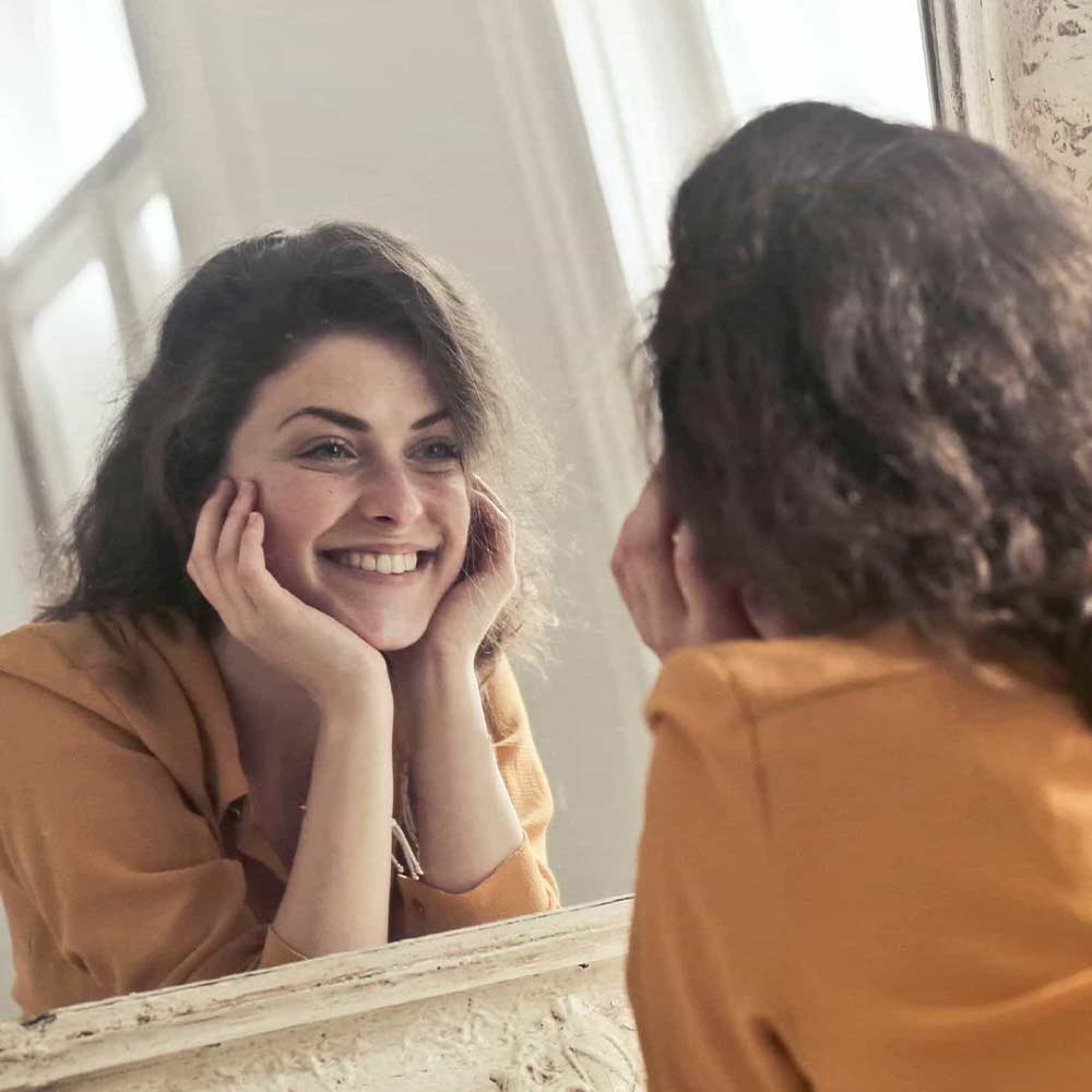 Eine junge Frau liegt vor einem Spiegel und lächelt ihr Spiegelbild an
